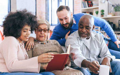 Multigenerational family sitting on a sofa reading a book together and enjoying quality time at home.